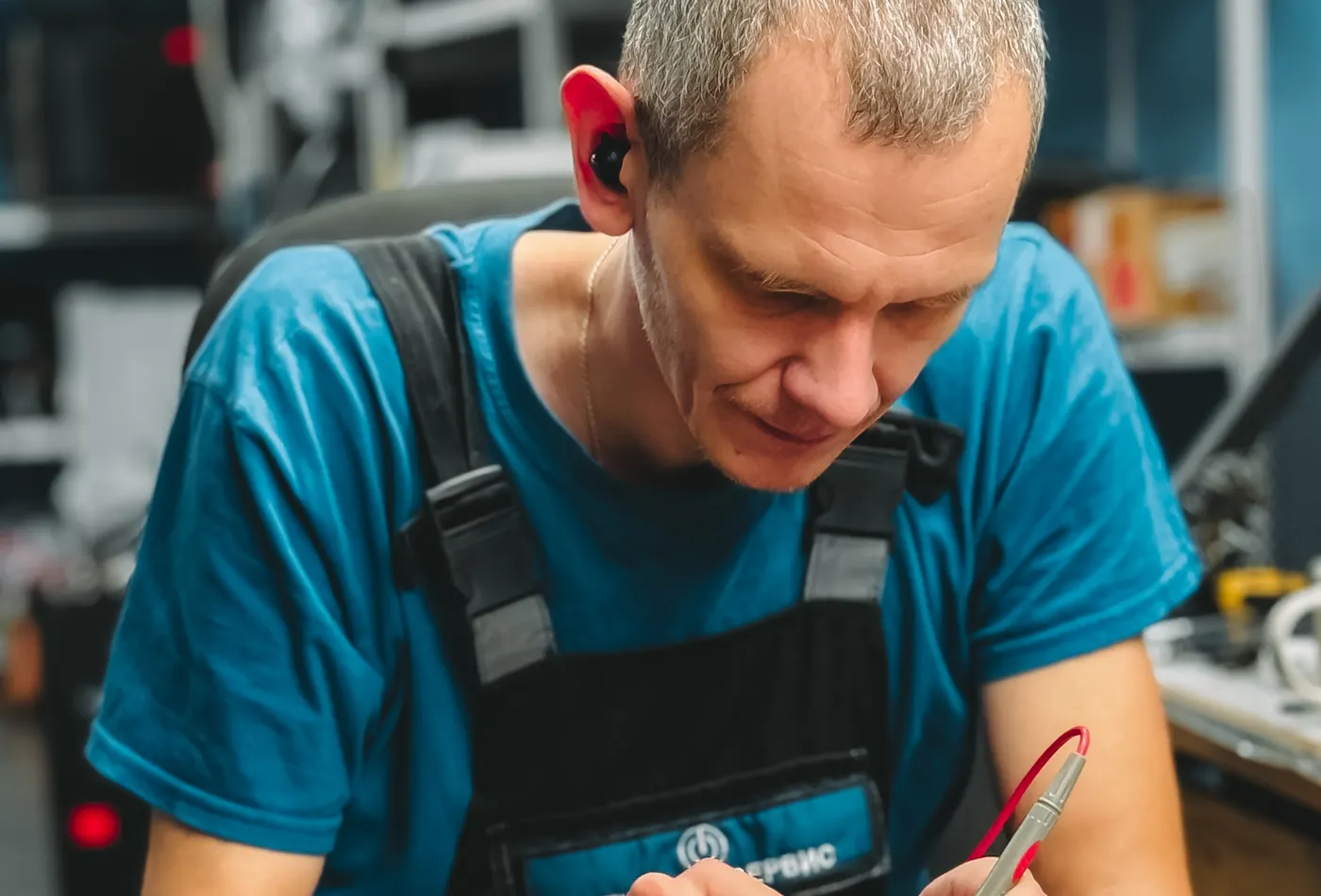 A repair technician at a lit workbench inspecting a laptop