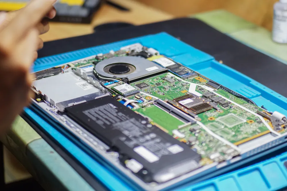 A laptop opened for maintenance with tools beside it