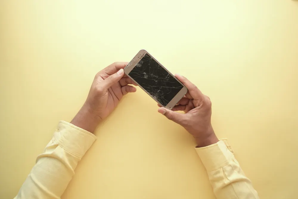 A person holding a smartphone with a badly cracked screen